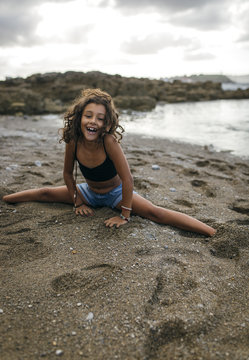Spain, Gijon, portrait of smiling little girl doing the splits on a beach