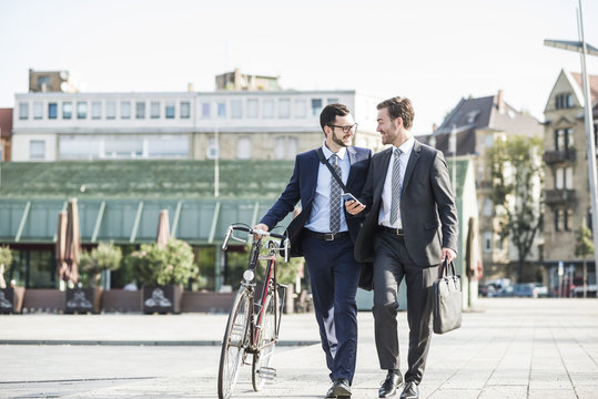 Two businessmen with bike and smart phone walking in the city