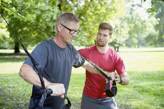 Man doing TRX training while his personal trainer watching him