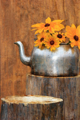 Sunflowers in a rustic teapot on a tree stump.