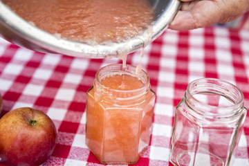 Senior woman pouring homemade applesauce in a jam jar, close-up