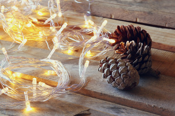 pine cones next to gold garland lights on wooden background. copy space
