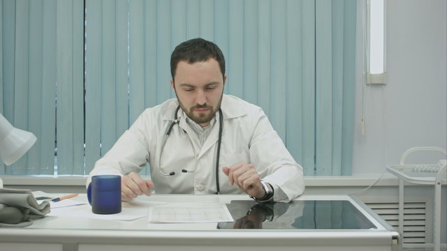 tired  from work, bearded doctor drink from cup and continue woking with documents and x-rays