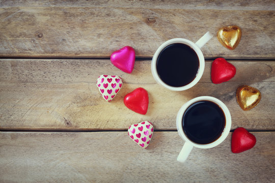 top view image of colorful heart shape chocolates and couple mugs of coffee on wooden table. valentine's day celebration concept. retro filtered image
