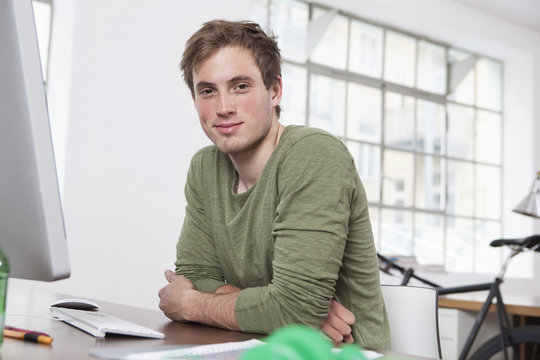 Portrait of smiling young man sitting at his desk in the office
