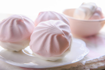 Still life in pastel colors with pink and white marshmallows on a white plate with a napkin.