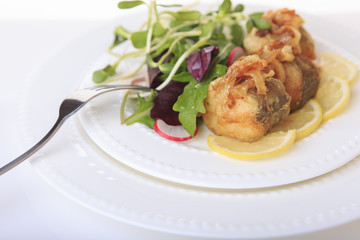 Fried fish with fried onions, lettuce and lemon on a white plate closeup.