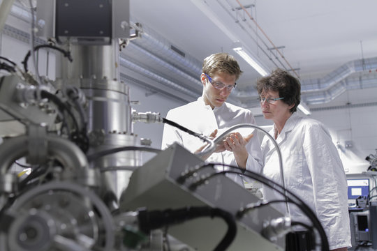 Two scientists standing in analytical laboratory with scanning electron microscope in foreground - Powered by Adobe