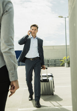Business man with rolling suitcase telephoning with smartphone