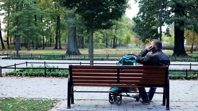 Man with stroller talking on cellphone in park

