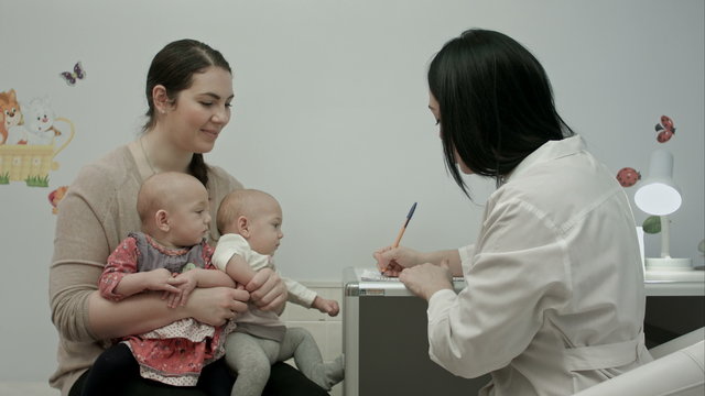 Cute newborn twins being examine by pediatrician with toy