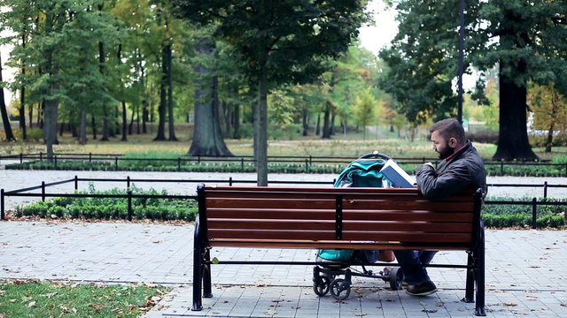 Man with stroller reading book in the park
