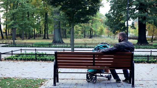 Happy man with stroller relaxing on bench in the park
