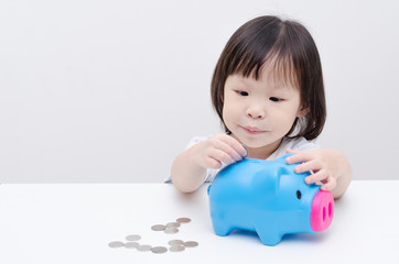 Little Asian girl insert coin into piggy bank
