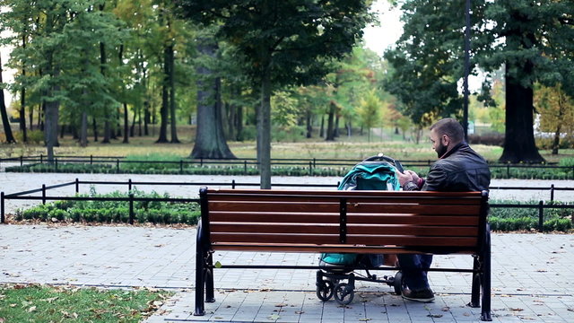 Man with stroller texting on smartphone on bench in the park
