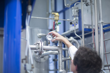 Woman with lab coat in technical room with a fermenter