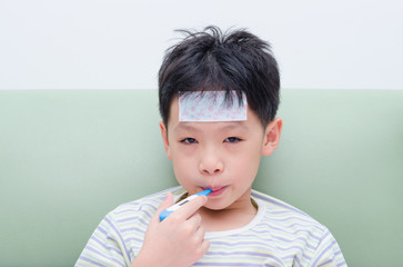 Little sick boy sitting on sofa with thermometer in mouth