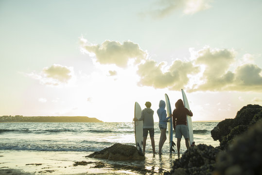 Three teenagers standing on the beach with their surfboards looking at horizon