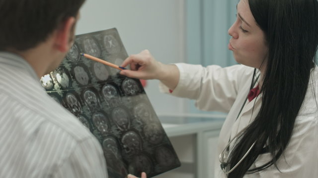 Female doctor in clinic show x-rays to male patient.