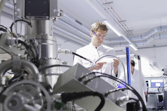 Scientist standing in analytical laboratory with scanning electron microscope in foreground