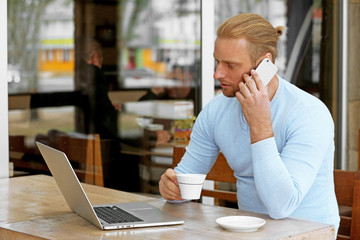 Young attractive businessman having lunch and working in a cafe