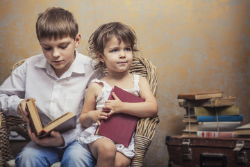 Cute babies boy and girl in a chair reading a book in a interior