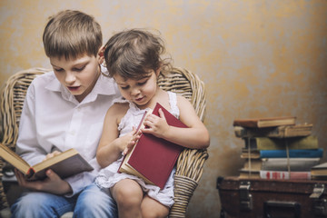 Cute babies boy and girl in a chair reading a book in a interior