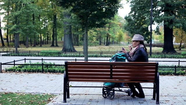 Woman with stroller applying lipstick on bench in park
