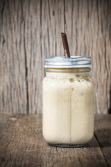 Iced coffee with milk in vintage jar on wood background