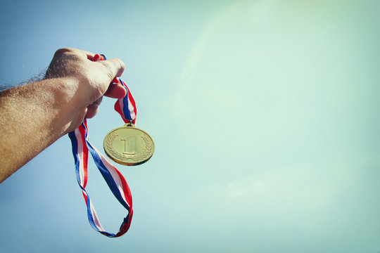 man hand raised, holding gold medal against skyl. award and victory concept. selective focus. retro style image.
