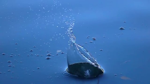 Close up scene of big stone falls into the calm blue water. Impressive moving background with meditative effect. Slow motion. Relaxing view of the calm water. Full HD footage 1920x1080.
