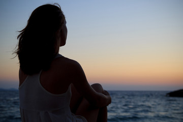 Woman silhouette watching sunset, sitting alone by the sea
