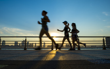 Motion blur silhouettes of joggers running at sunset on the Hudson River boardwalk in New York City