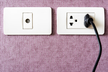 black cable plugged in a white electric outlet mounted on pink w