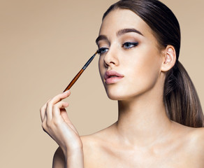 Fototapeta premium Enchanting young girl with brush for eyeshadow / photoset of attractive brunette girl on beige background
