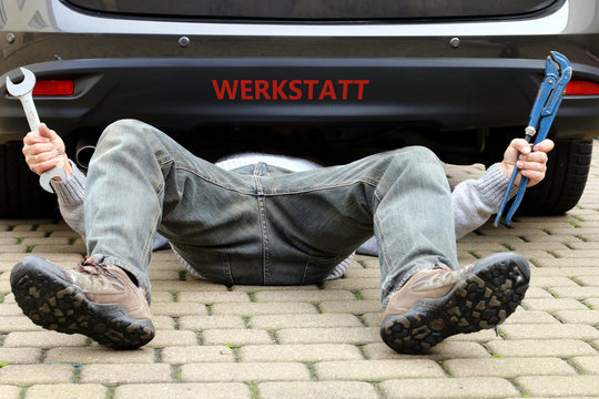 Mann unter Auto "Werkstatt" an Stoßstange