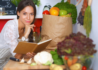 Young woman reading cookbook in the kitchen, looking for recipe