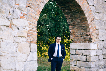 Fototapeta na wymiar confident, cute groom man in a stylish business suit, outdoors, autumn. Portrait of the groom in the park on their wedding day. Rich groom man on their wedding day
