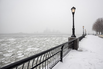 Naklejka premium Frozen Hudson River from snowy Battery Park towards Jersey City in fog. A silent winter day in New York City.