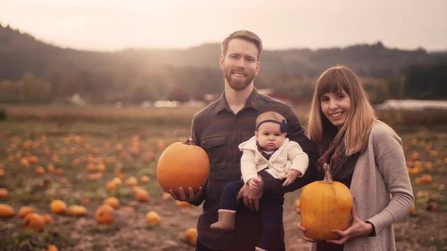 Portrait of a young family at a pumpkin patch, mom and dad holding pumpkins, with lens flare