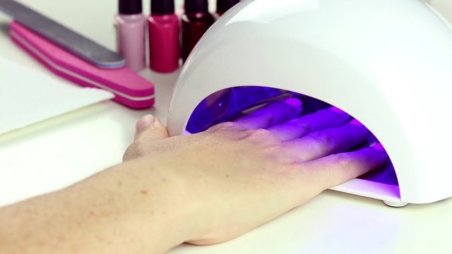 Manicure in process - putting hand and curing gel varnish in nail LED lamp, procedure of polymerization