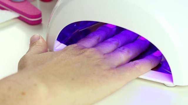 Manicure in process - putting hand and curing gel varnish in nail LED lamp, procedure of polymerization