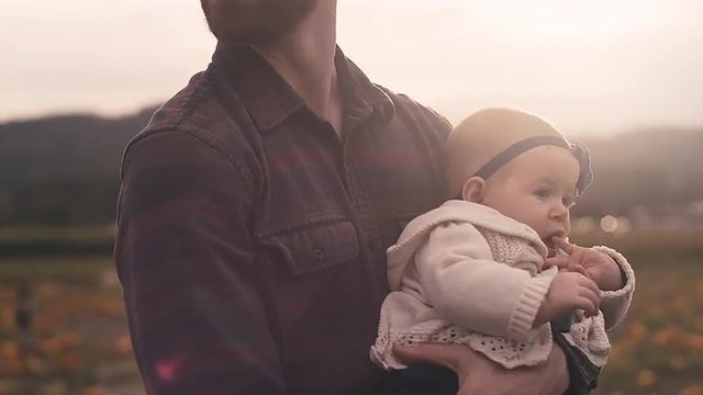 A young man holding his baby at a pumpkin patch on a fall day, with lens flare
