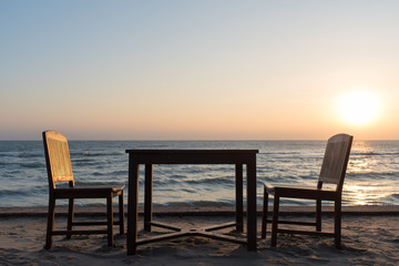 Wooden chairs on the beach at sunrise with a tropical sea background
