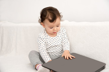Cute baby girl playing with a laptop at home