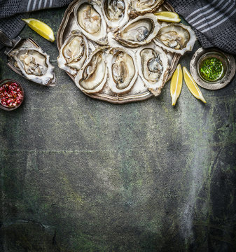 Opened oysters with lemon and various sauces  on rustic background, top view, place for text