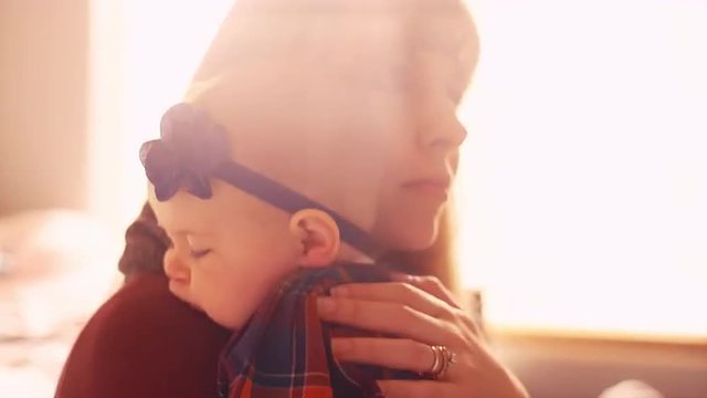 A young mother bouncing her baby to sleep on a yoga ball, with lots of window light