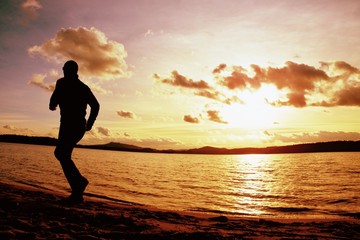 Fototapeta na wymiar Tall sportsman run along sea coast of sunrise behind, empty beach