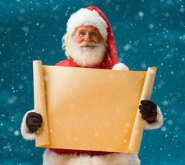 Santa Claus holding vintage paper blank sign / Winter night with snowfall. Closeup on blurred blue background.