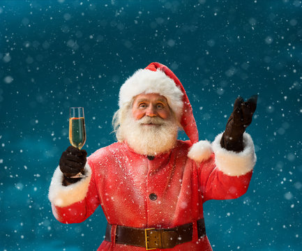 Santa Claus with a glass of champagne and looking at camera / Merry Christmas & New Year's Eve concept / Closeup on blurred blue background.